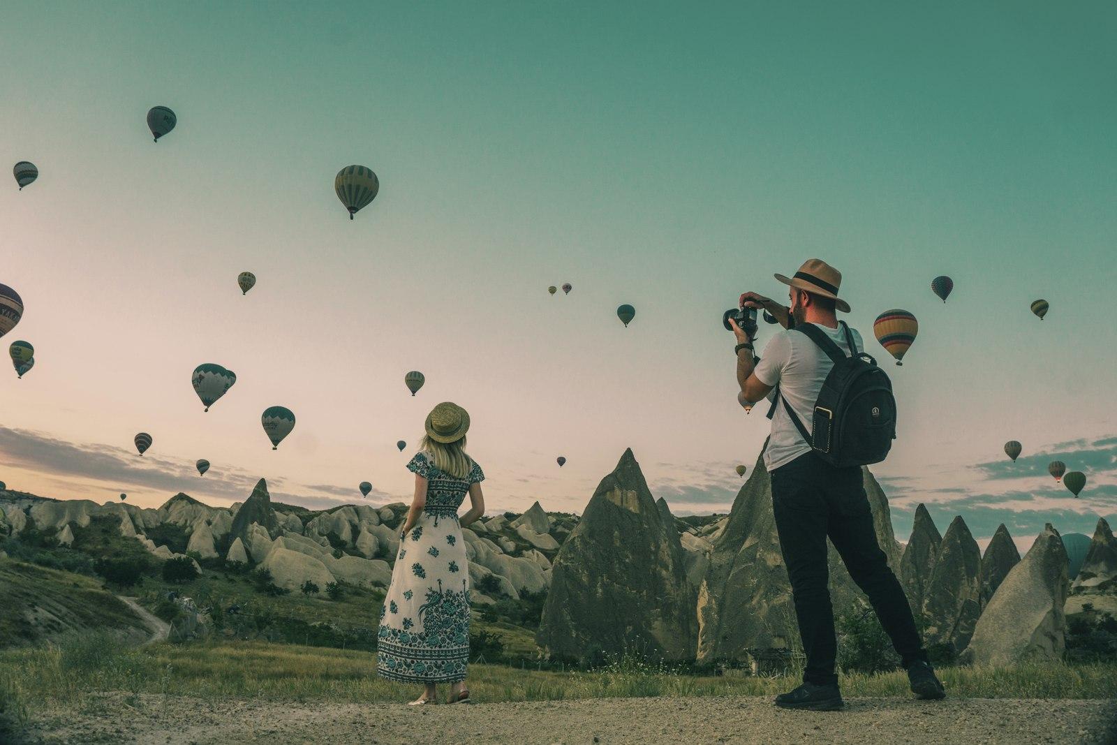 Couple watching hot-air balloons rise over a valley at sunrise